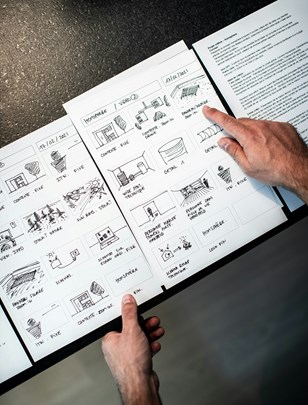 Storyboard sketches and content planning documents spread across a table, with people reviewing layouts and visual concepts for digital communication materials.