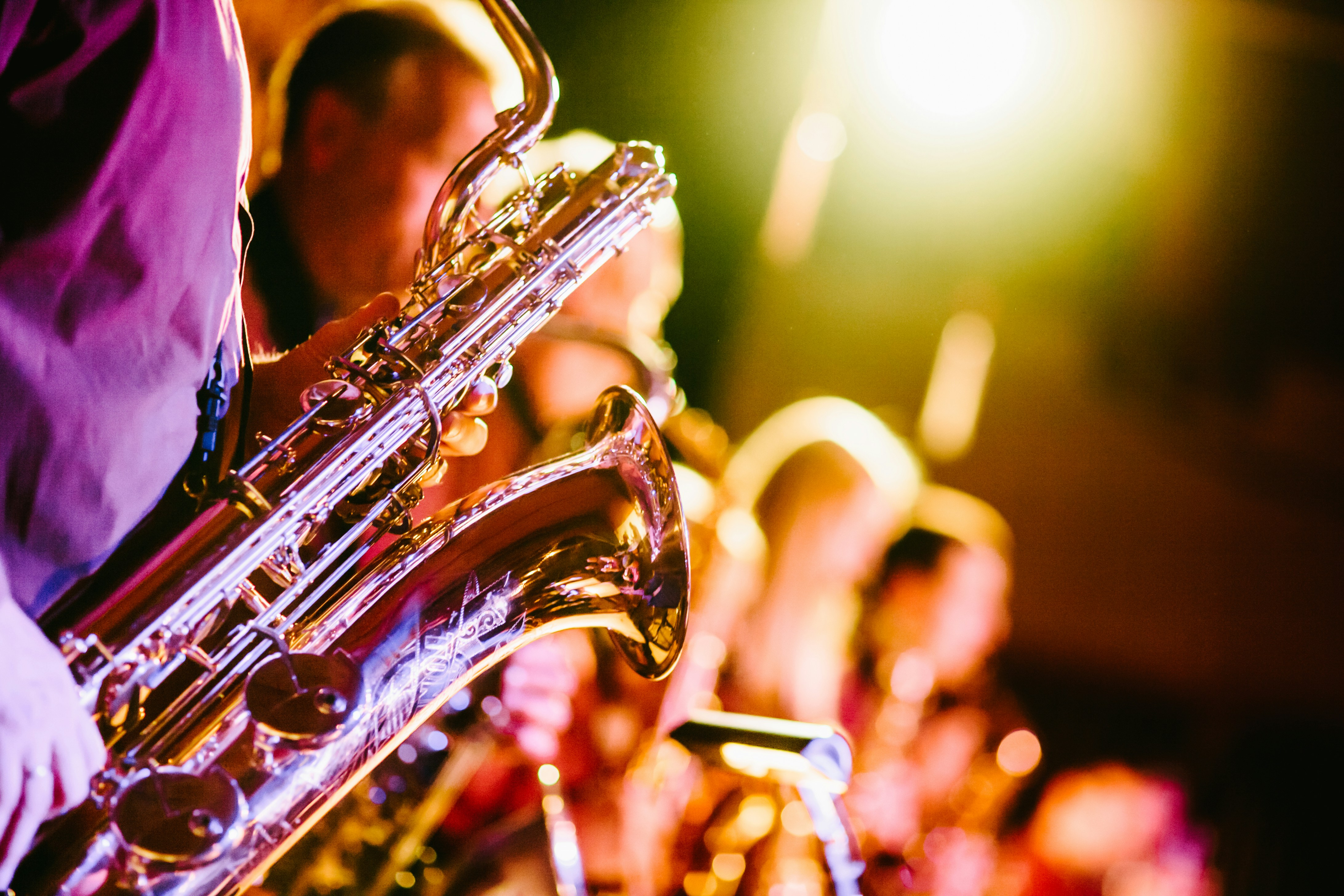Musicians playing saxophones in a vibrant, warmly lit setting, with blurred background and bright stage lights.